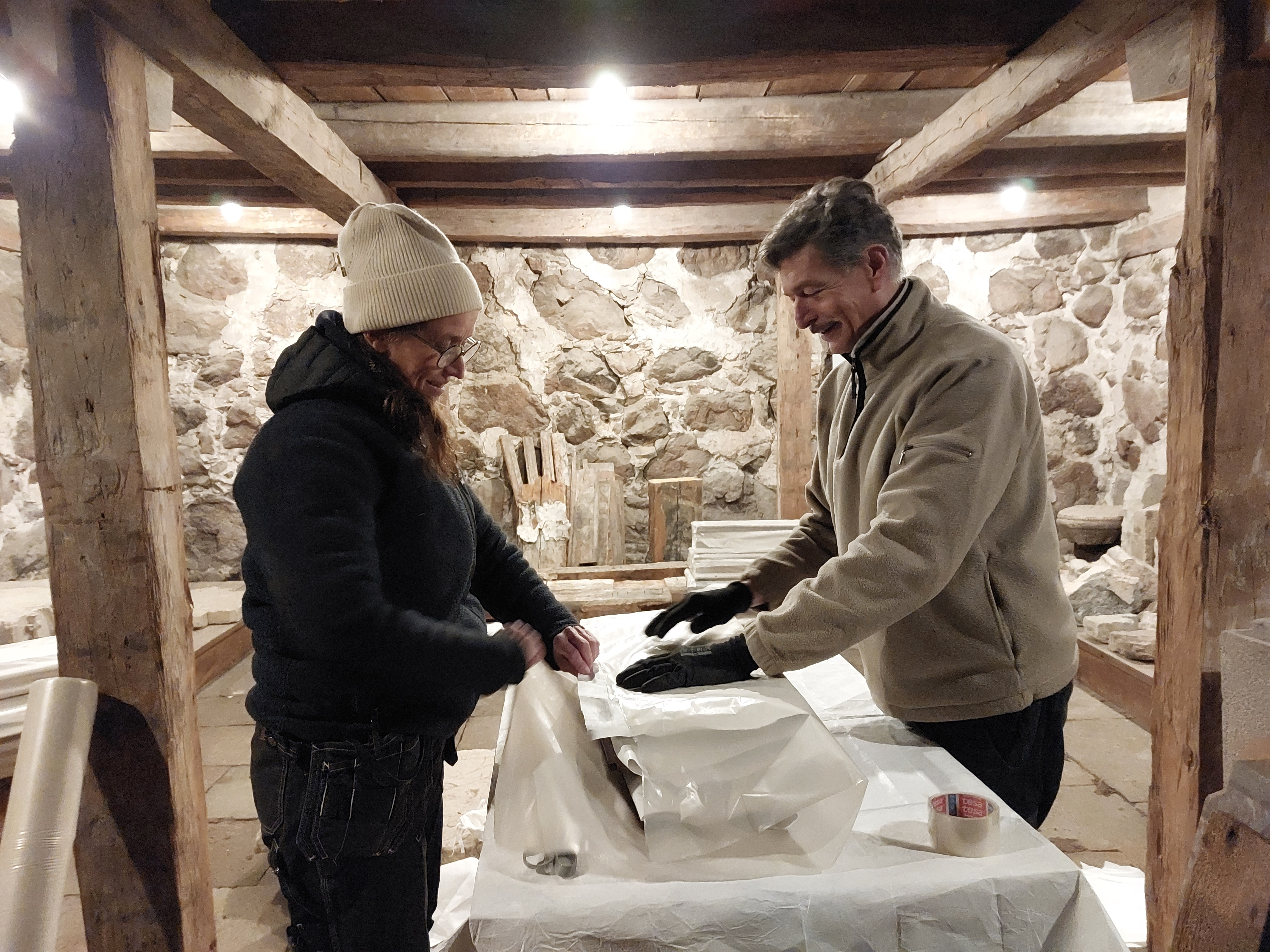 Föremål av sten, trä och järn flyttas från det medeltida stenhuset Rhyzeliusgården i Linköping till ett av museets magasin. Här ses konservatorerna Johanna Palm-Avis och Johan Roos.