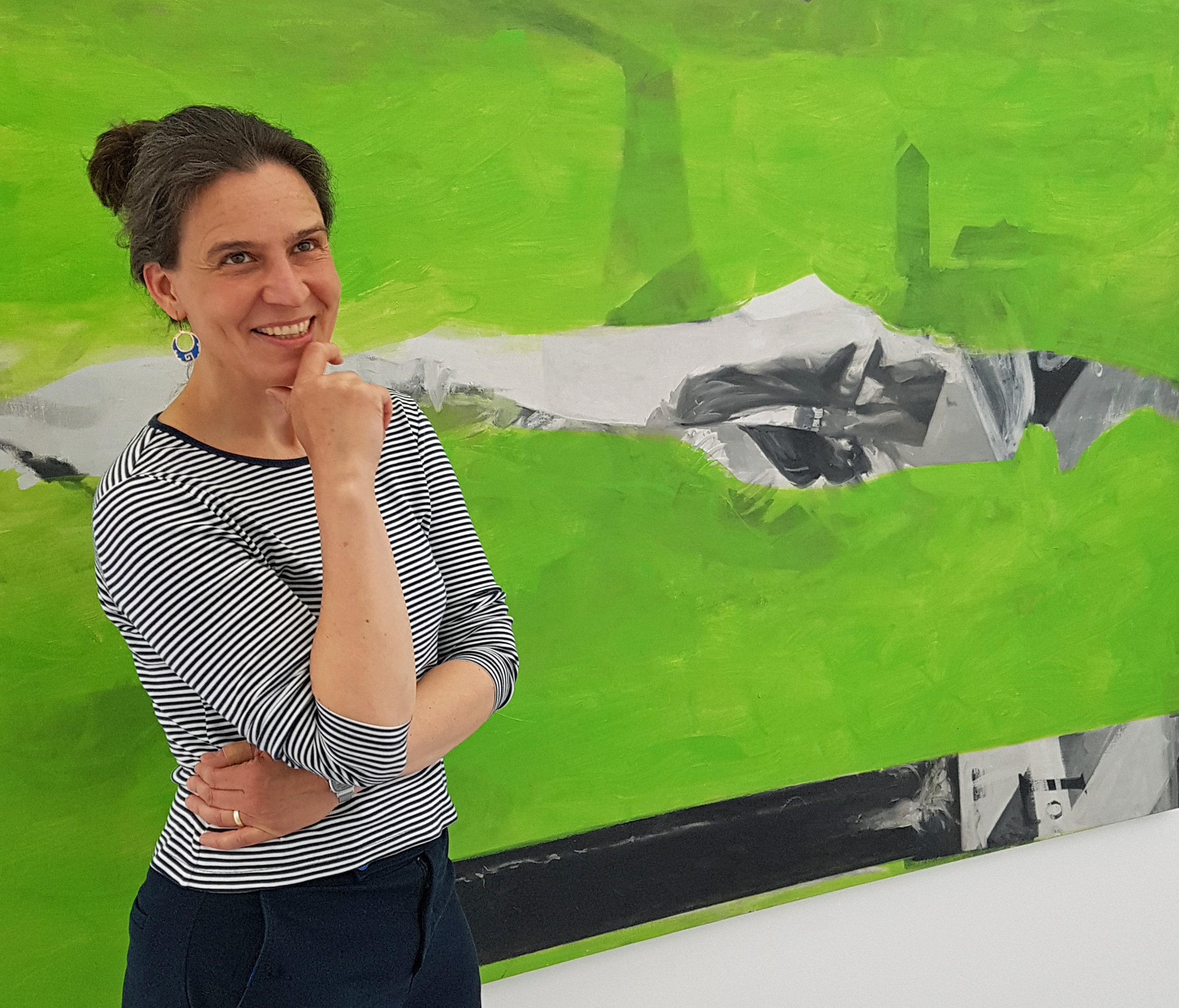 Konstintendent Melanie Klein framför en målning i grönt, svart och vitt, i konstutställningen