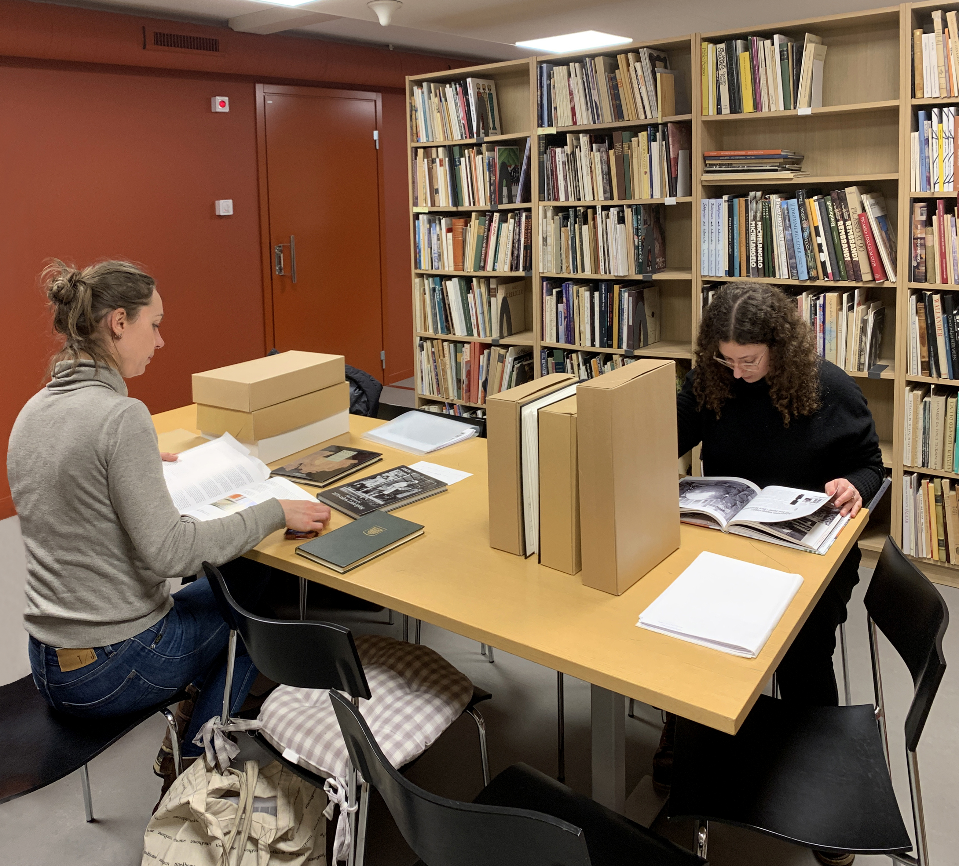 Två arkivanvändare sitter med handlingar och böcker i biblioteket