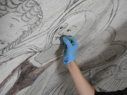 En hand som rengör en äldre takmålning.