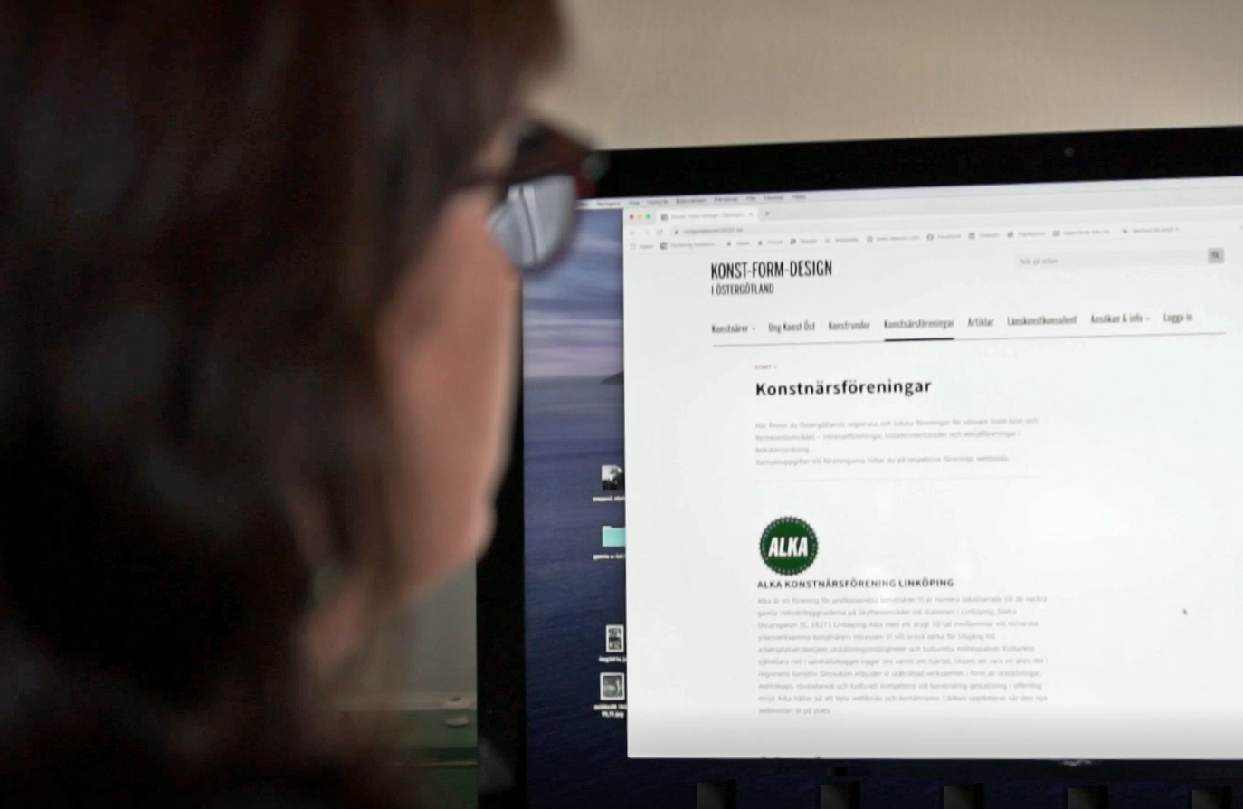 En leende länskonstkonsulent Lena Wiklund framför sin dator med webbsidan Konst Form-Design i Östergötland