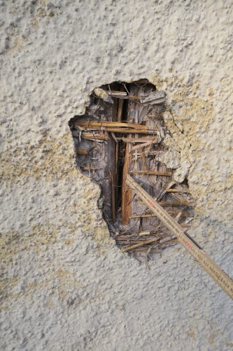 Detaljbild på en sprucken fasad genom vilken träpanelen syns igenom.