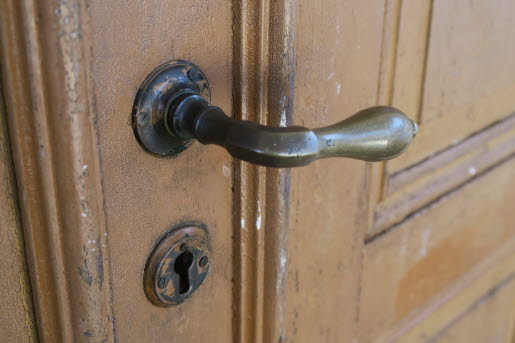 Detaljbild på ett äldre dörrhandtag på en trädörr.