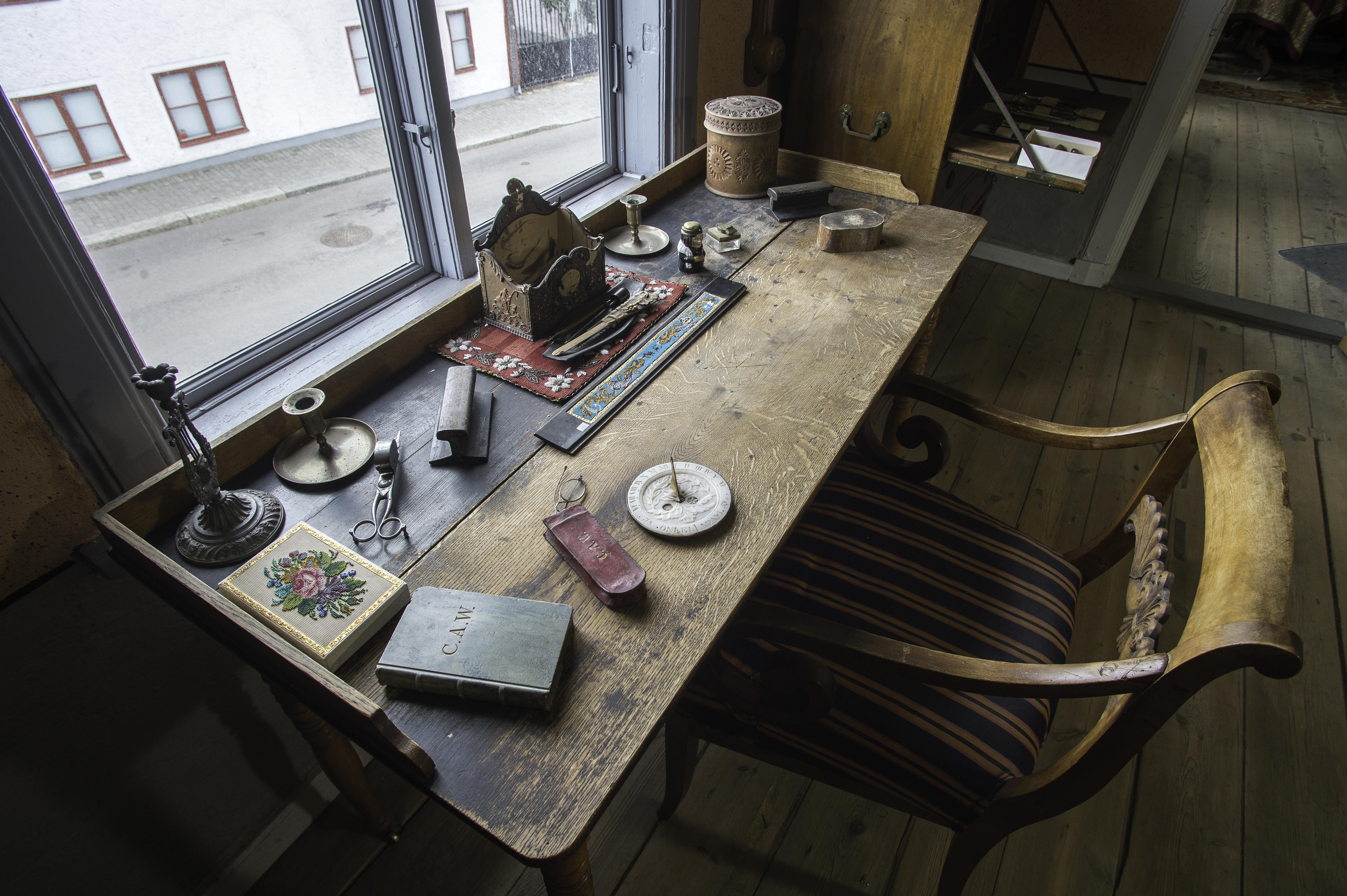 Interiör i museilägenheten i Onkel Adamsgården med bland annat ett skrivbord och en skrivbordsstol. Framför skrivbordet ett fönster med utsik mot huset på motstående sida av gatan.