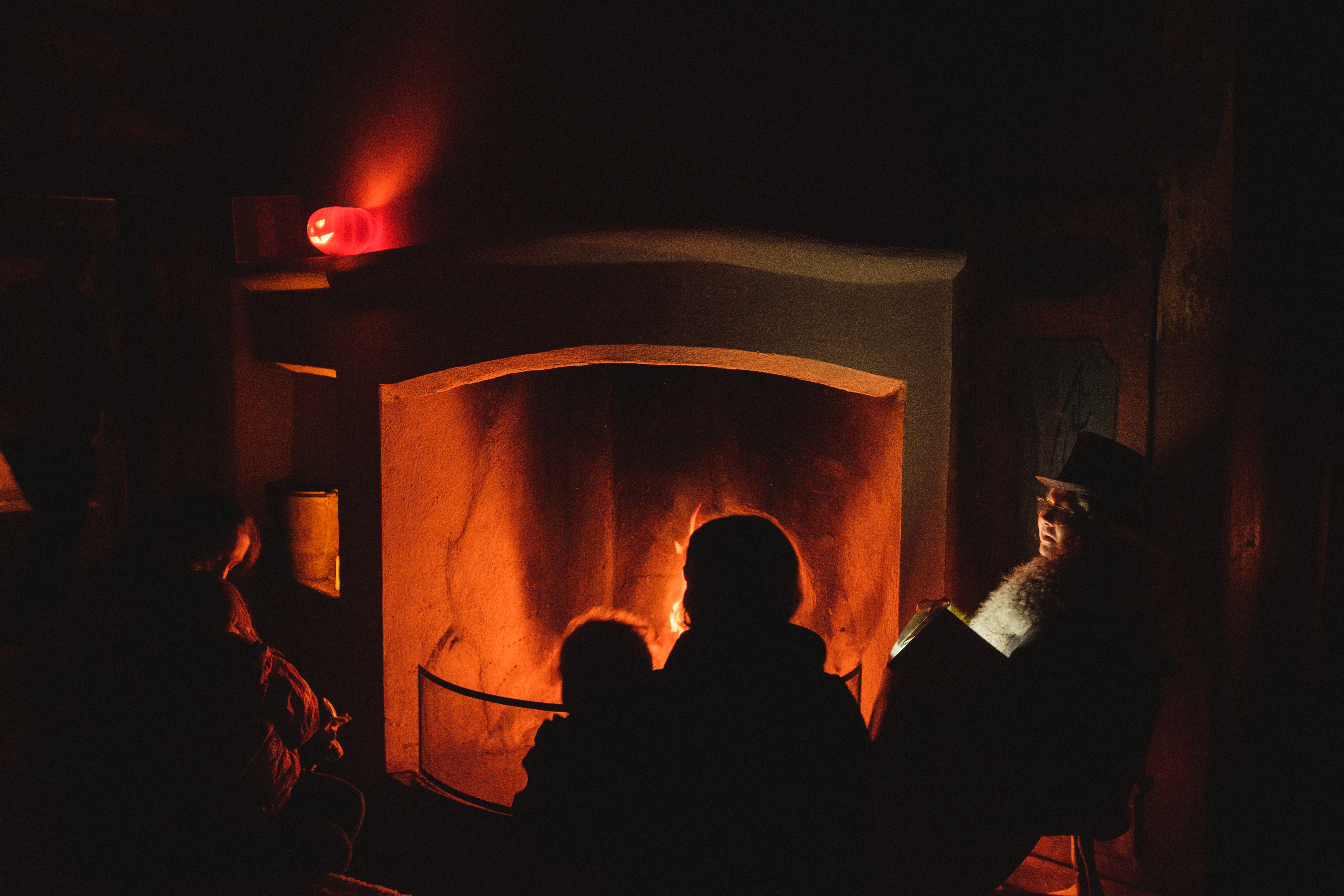 En person i hatt berättar sagor för barn framför en eldstad. Det är kväll och elden brinner.