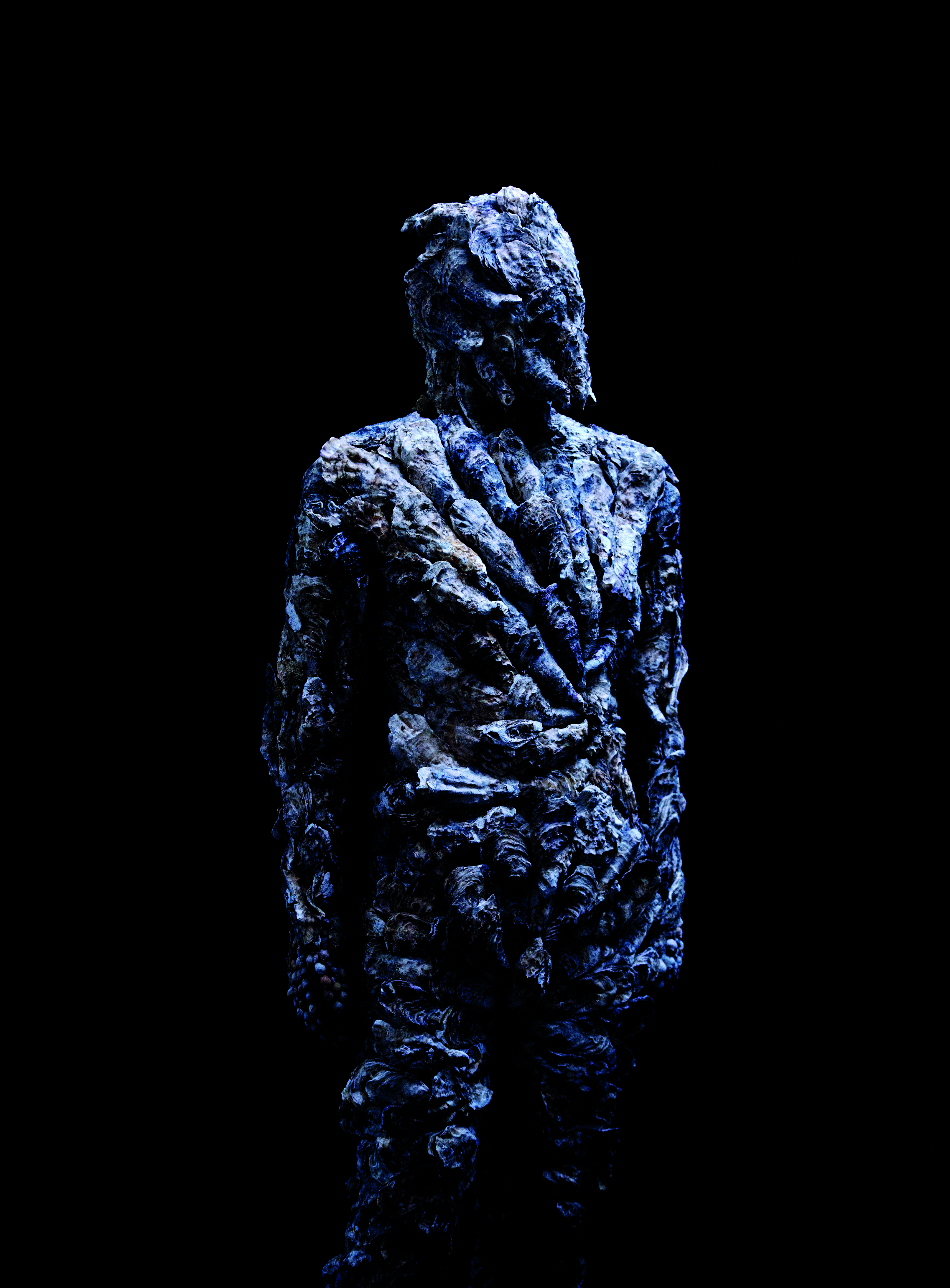 Huvud och överkropp av människoliknande varelse som istället för hud och ansikte täcks av en kraftigt skrovlig yta i blågrått.